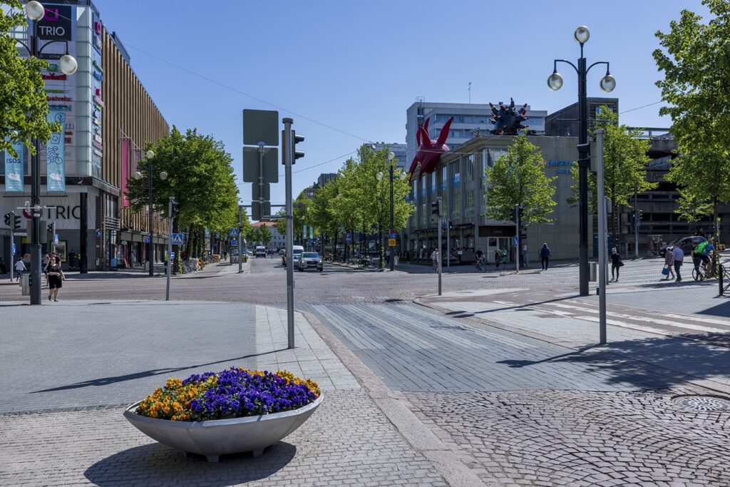 A summer cityscape with a red and black inflatable artwork on the building’s roof on the right.