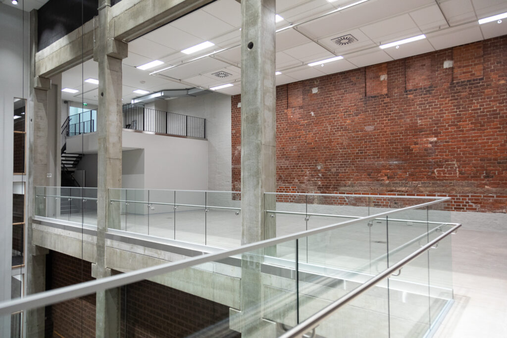A light space with a red‑brick wall, three concrete pillars, and a glass railing.