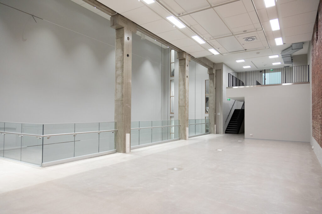 A light interior space dominated by three concrete pillars and a glass railing.