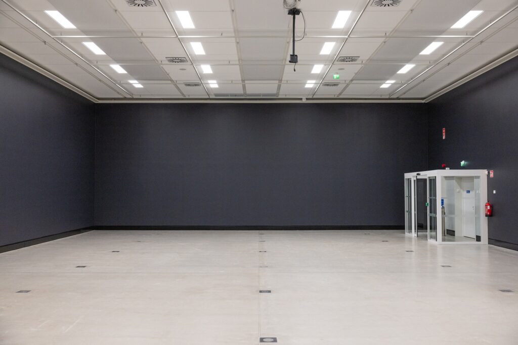 A dark‑walled interior space with a grey floor and bright ceiling lights.