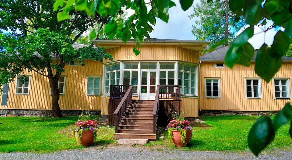 Matala keltainen puurakennus puiden takana.